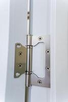 This is a closeup view of a stainless steel door hinge attached to a contemporary white door frame, showcasing its sleek design and functionality photo