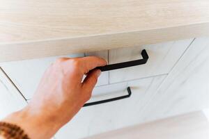 A person is using a gesture to open a drawer with a black hardwood handle photo