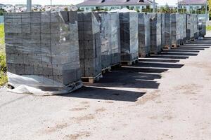 Pallets of neatly arranged concrete paving blocks at construction site for new building development, outdoor storage of heavy materials, wrapped in microwave wrap for future housing project photo