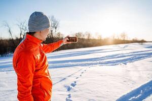 Man taking selfie on smartphone while standing on snow in winter forest, taking pictures of himself, self-portrait, winter outdoor recreation. photo