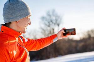 Man taking selfie on phone while standing in winter forest, guy taking pictures of himself on smartphone, landscape photography. photo