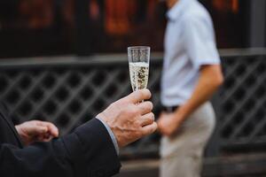 Man gesturing with glass of champagne at another man at event photo