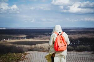 A person with a red backpack is strolling down the sidewalk under a cloudy sky photo