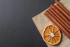 Cinnamon sticks bundle. Dried orange slice and cinnamon sticks on a dark surface. photo