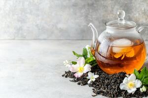 Floral iced tea. Glass teapot with brewed tea and flowers on a gray background. photo