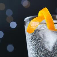 Shimmering cocktail glass. Refreshing drink with orange peel against a bokeh background. photo