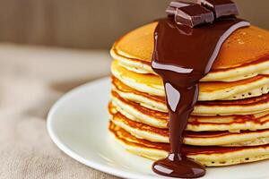 Smooth chocolate drip. Stack of pancakes drizzled with chocolate sauce on a white plate. photo