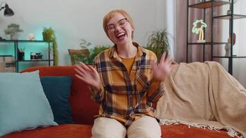 Pretty woman smiling friendly at camera, waving hands gesturing hello, hi, greeting at home on sofa video