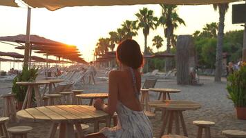 Young Woman Enjoying Sunset While Sitting on Beach Table in Warm Sunlight video