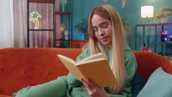 Young woman relaxing interesting book turning pages smiling enjoying literature taking rest on sofa video