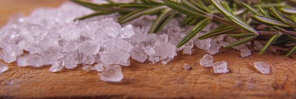 Coarse sea salt and fresh rosemary on wooden surface for culinary concepts photo