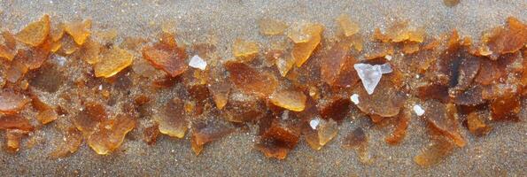 Brown glass shards on sandy beach, glimmering fragment textures close-up photo