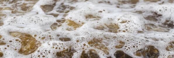 Close-up view of sea foam and bubbles forming over brown pebbles near shore photo