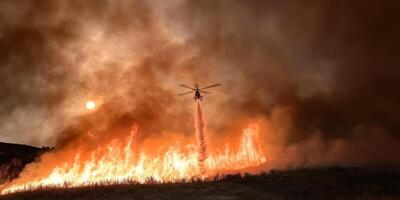 Helicopter dropping water on intense wildfire under smoky orange sky photo
