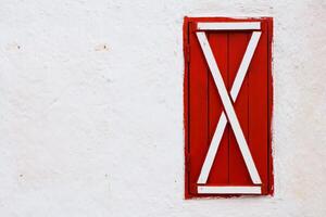 The bright and vibrant red shutter beautifully graced by an elegant white wall structure photo