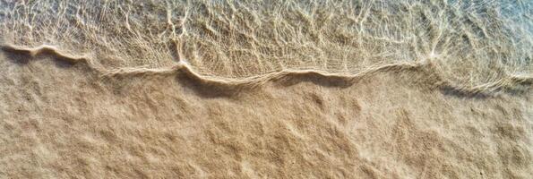 Tranquil shoreline with rippling waves and sandy texture in natural light photo