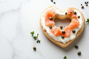 A gourmet heart-shaped bagel is beautifully spread with cream cheese and adorned with slices of smoked salmon and capers photo