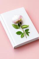 Simple and elegant mockup of a blank white book cover adorned with a flower and leaves on a peach background photo