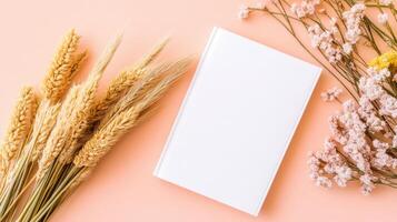 Mockup of a blank white book cover surrounded by dried flowers against a peach-colored background highlighting simplicity and elegance photo
