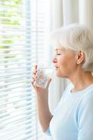 Older woman enjoying a refreshing glass of water while relaxing in a bright home environment with a serene expression photo