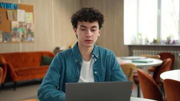 Concentrated serious Caucasian teen man male guy student schoolboy pupil using laptop computer e-learning learn studying online internet web pc task education in school university homework prepare video