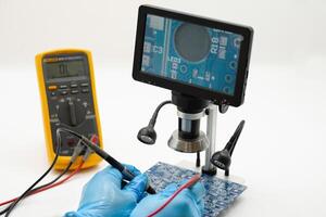 Closeup examination of a circuit board using a digital microscope and multimeter in a workshop photo