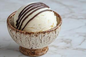 A scoop of vanilla ice cream with chocolate drizzled on top in a small bowl photo