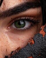 Closeup of a womans eye with green iris, partially obscured by dark, textured material photo