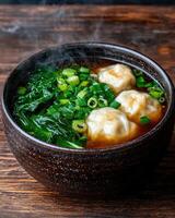 Steaming bowl of wonton soup with spinach and green onions photo
