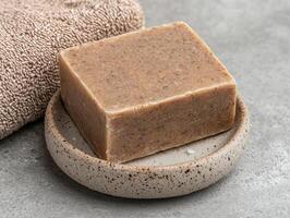A bar of natural soap sits on a rustic soap dish next to a towel photo