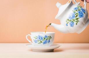 Old-style porcelain kettle pouring tea from jug to cup of tea photo
