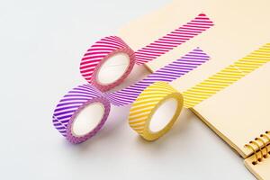 Colorful striped tape rolls displayed with a notebook on a clean surface photo