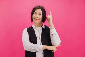 Smiling businesswoman pointing up with index finger on pink background photo