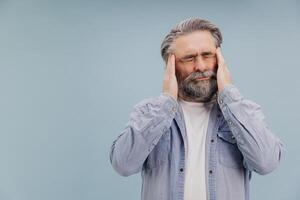 Senior man suffering from headache touching temples with hands on blue background photo