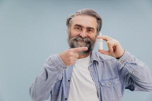 Senior man holding nasal spray and pointing on it photo