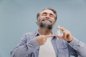 Senior man holding nasal spray and pointing at it with index finger photo