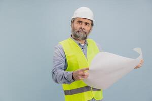 Senior engineer wearing safety helmet and vest pointing at blueprint on blue background photo