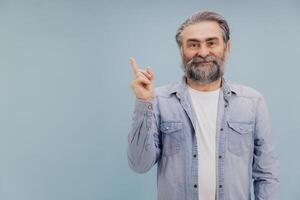 Smiling senior man pointing up with index finger on blue background photo