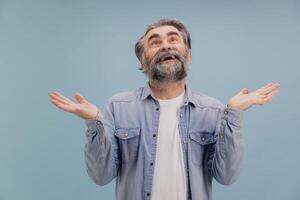 Surprised senior man shrugging shoulders with open palms looking up on blue background photo