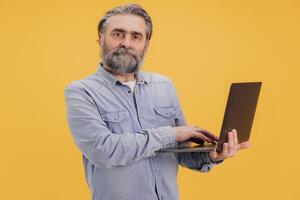 Senior programmer working on laptop standing on yellow background photo