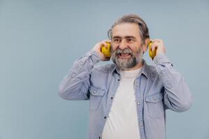 Smiling Senior Man Enjoying Music with Yellow Headphones on Blue Background photo