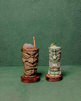 Refreshing Drinks In Two Tiki God Glasses, Elegantly Served On Round Wooden Coasters, Offering A Stylish And Tropical Vibe. photo