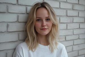 Young woman with wavy blond hair poses against a textured white brick wall in a well-lit indoor setting photo
