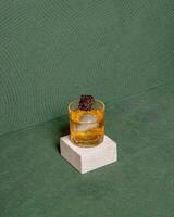 Glass Of Cocktail Featuring A Round Ice Sphere, Topped With A Decorative Dark Brown Garnish, Elegantly Presented On A Minimalist White Block. isolated on green texture background photo
