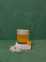 A Cocktail Glass Featuring A Round Ice Ball, Topped With A Decorative Garnish, Elegantly Served On A Minimalist White Block With Flowers. photo
