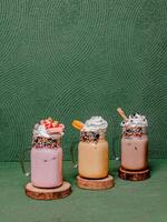 Delicious Strawberry, Mocha, And Chocolate Milkshakes With Whipped Cream And Toppings, Elegantly Served In A Glass On A Round Wooden Coaster. photo