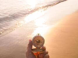 Close-up hand holding compass with beach background in the sunset time photo