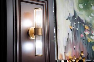 A wall light with a gold finish and a painting on the wall photo