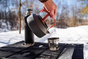A person pours water into a cup on a camping stove photo
