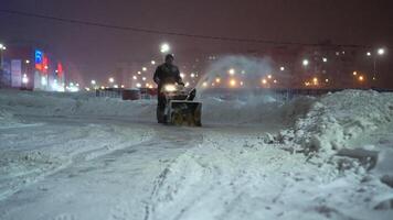 Snow removal with a snow thrower in the evening in an amusement park. A man drives a harvesting manual tractor throwing snow from the track video